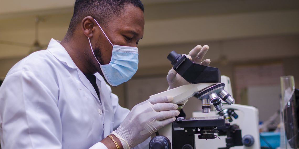 young handsome african scientist in the lab carefully carrying out experiments while using a microscope