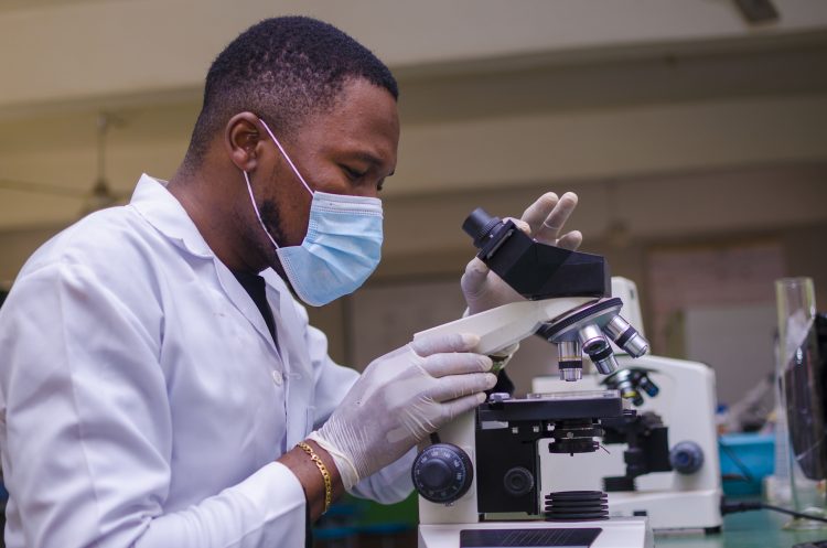 young handsome african scientist in the lab carefully carrying out experiments while using a microscope