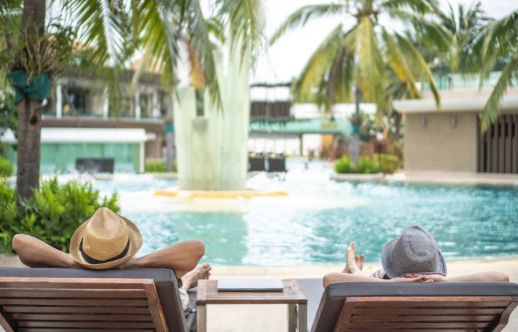Summer resort hotel stay relaxation with tourist traveller couple take it easy happily resting on beach chair on holiday travel vacation poolside peacefully at tropical beach swimming pool