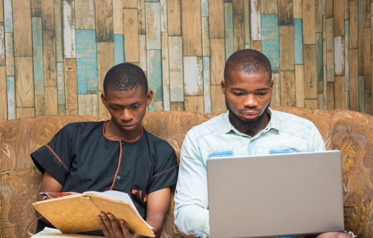 a young african businessman holding record book while his friend check it on his laptop