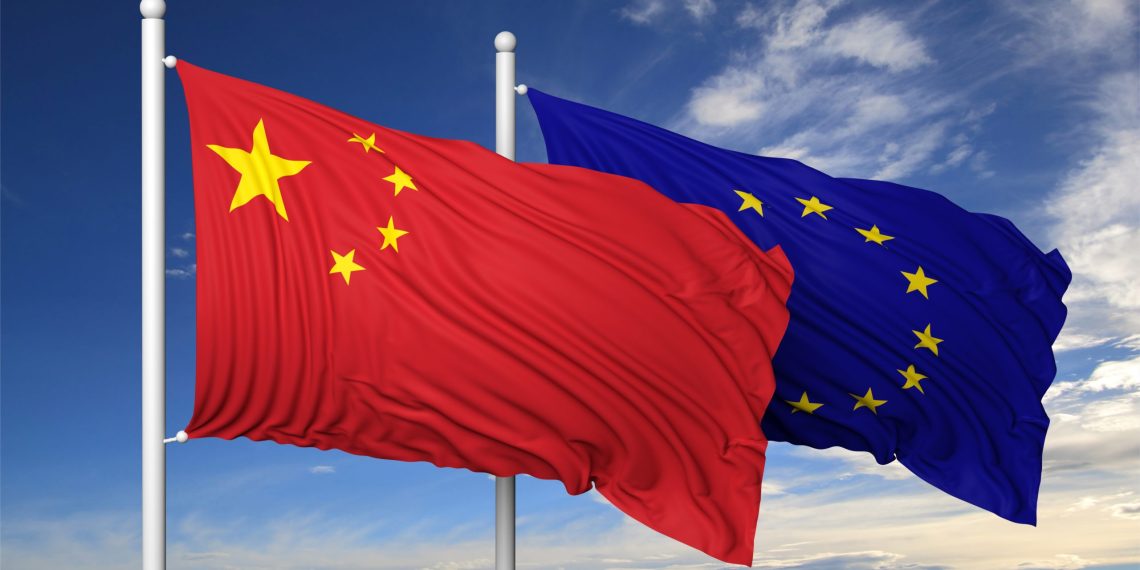 Waving flags of China and EU on flagpole, on blue sky background.